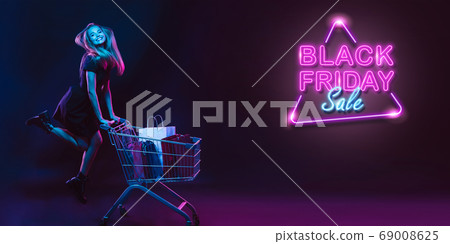 Portrait of young woman in neon light on dark backgound. The human emotions, black friday, cyber monday, purchases, sales, finance concept. Neoned lettering. Portrait of young woman in neon light on dark backgound. The human emotions, black friday, cyber monday, purchases, sales, finance concept. Neoned lettering. 69008625