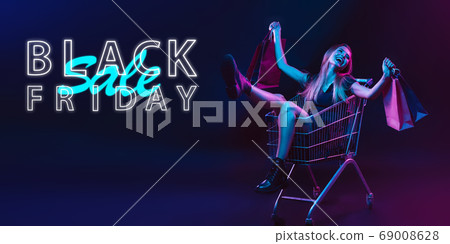 Portrait of young woman in neon light on dark backgound. The human emotions, black friday, cyber monday, purchases, sales, finance concept. Neoned lettering. Portrait of young woman in neon light on dark backgound. The human emotions, black friday, cyber monday, purchases, sales, finance concept. Neoned lettering. 69008628