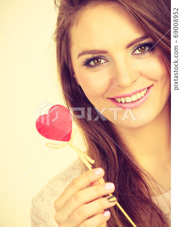 Flirty woman holding red wooden heart on stick 69008952