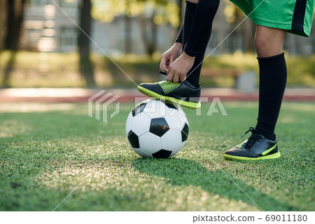 Close up boot of football player which puts his leg on ball and tying shoelace on soccer stadium on the training. Close up boot of football player which puts his leg on ball and tying shoelace on soccer stadium on the training. 69011180