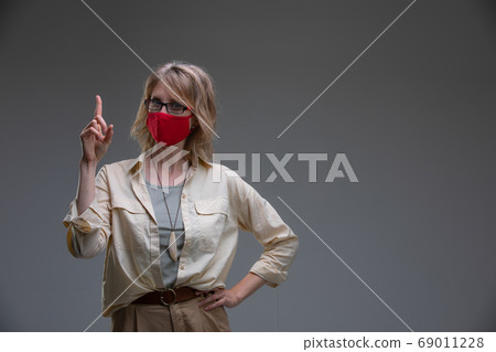 Blond young female in red protective mask against viruses, holds her head. 69011228