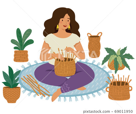 Woman weaving DIY baskets on the ground with handmade wicker baskets and plants around her 69011950