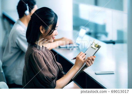 休閒服裝回答問卷的年輕女商人在辦公室 休閒服裝回答問卷的年輕女商人在辦公室 69013017