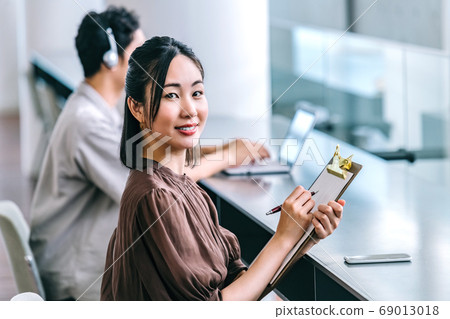 休閒服裝回答問卷的年輕女商人在辦公室 休閒服裝回答問卷的年輕女商人在辦公室 69013018