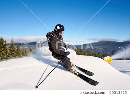 Man skiing on prepared slope with fresh snow. Snow gun machine making artificial snowfall. Magic nature on background. Man skiing on prepared slope with fresh snow. Snow gun machine making artificial snowfall. Magic nature on background. 69013315