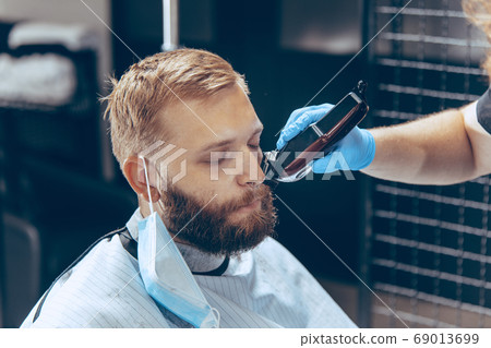 Man getting hair cut at the barbershop wearing mask during coronavirus pandemic Man getting hair cut at the barbershop wearing mask during coronavirus pandemic 69013699