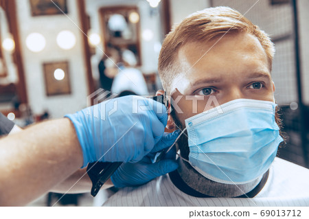Man getting hair cut at the barbershop wearing mask during coronavirus pandemic Man getting hair cut at the barbershop wearing mask during coronavirus pandemic 69013712