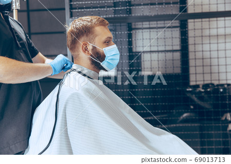 Man getting hair cut at the barbershop wearing mask during coronavirus pandemic Man getting hair cut at the barbershop wearing mask during coronavirus pandemic 69013713