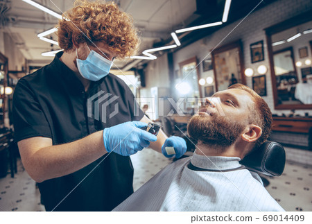 Man getting hair cut at the barbershop wearing mask during coronavirus pandemic 69014409