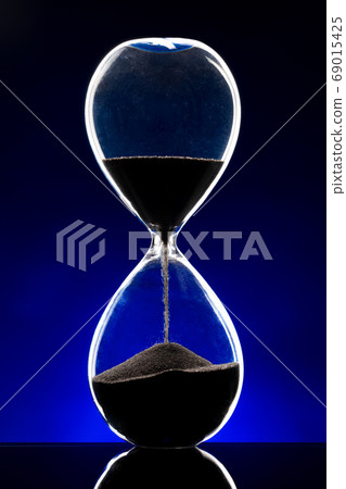 Hourglass illuminated on dark blue background close up 69015425