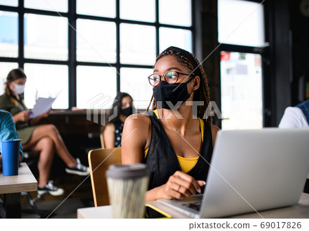 Portrait of young businesswoman with face mask working indoors in office. 69017826