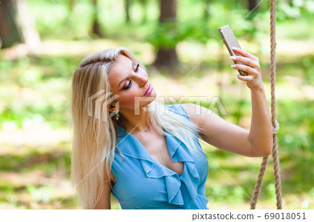 Beautiful blond woman in blue dress using smartphone to taking selfie Beautiful blond woman in blue dress using smartphone to taking selfie 69018051