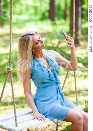 Beautiful blond woman in blue dress using smartphone to taking selfie Beautiful blond woman in blue dress using smartphone to taking selfie 69018052
