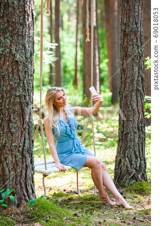 Beautiful blond woman in blue dress using smartphone to taking selfie Beautiful blond woman in blue dress using smartphone to taking selfie 69018053