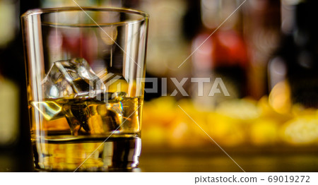 glass of whiskey with ice cubes and salty snacks 69019272