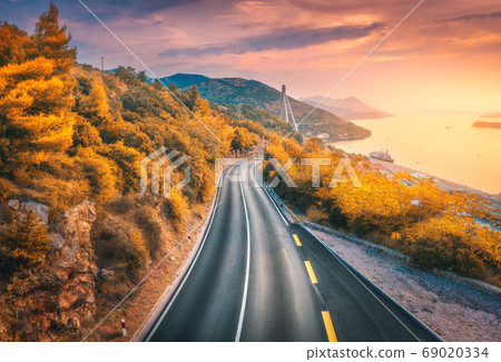 Aerial view of mountain road and beautiful orange forest at colorful sunset in autumn Aerial view of mountain road and beautiful orange forest at colorful sunset in autumn 69020334