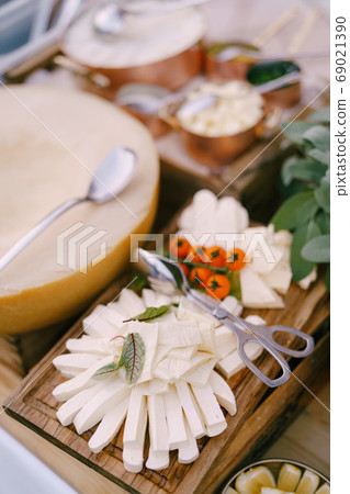 Melted cheese and a sprig of cherry tomatoes on a wooden plank with a melon on a blurred background. Melted cheese and a sprig of cherry tomatoes on a wooden plank with a melon on a blurred background. 69021390