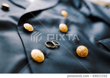 Two gold wedding rings on a blue men's jacket with buttons with a double-headed eagle. Two gold wedding rings on a blue men's jacket with buttons with a double-headed eagle. 69021392