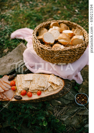 Wicker basket of bread on a bed on the ground with a wooden stand and biscuit biscuits, tomatoes and ham on it. Wicker basket of bread on a bed on the ground with a wooden stand and biscuit biscuits, tomatoes and ham on it. 69021394