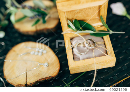 Open wooden box with wedding rings and a wooden stand with earrings and a chain with a pendant. 69021396