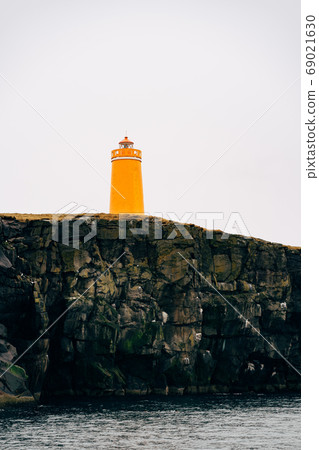 A huge orange lighthouse on a cliff in Iceland. 69021630