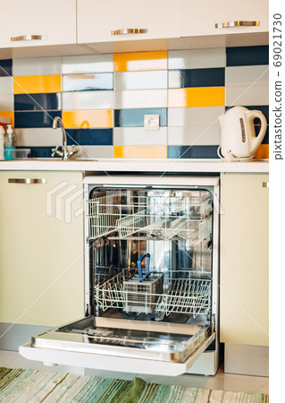 An open, empty dishwasher in a white kitchen decorated with blue, yellow and white tiles. An open, empty dishwasher in a white kitchen decorated with blue, yellow and white tiles. 69021730