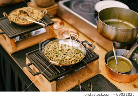 Frying pans with spaghetti on a cast iron stove in the kitchen. Frying pans with spaghetti on a cast iron stove in the kitchen. 69021825
