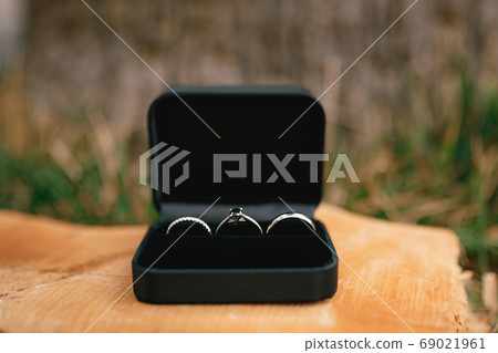 Wedding rings in white gold and an engagement ring in a black velvet box on a wooden base. 69021961