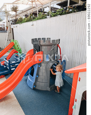 A little girl plays on the playground near a plastic castle and a children's slide. 69022292