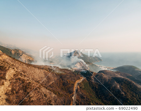 The city on the coast of Montenegro is engulfed in fire. White smoke over the city, the road and the mountains. The city on the coast of Montenegro is engulfed in fire. White smoke over the city, the road and the mountains. 69022490
