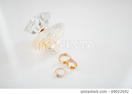Gold wedding rings and a gold engagement ring on a white background with a bottle of perfume. 69022692