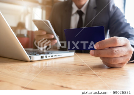 Businessman hand holding credit card and use laptop and smartphone in office. 69026881