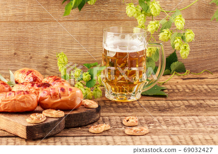 Fried sausages on wooden chopping board and glass of beer on wooden background Fried sausages on wooden chopping board and glass of beer on wooden background 69032427