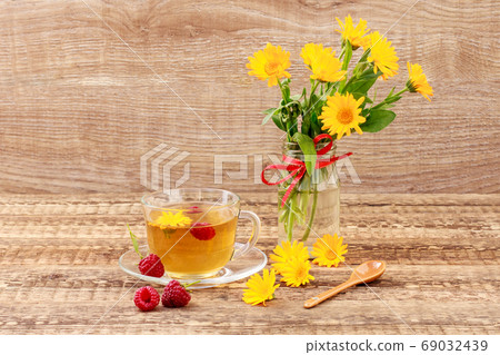 Glass cup of green tea with flowers of calendula and fresh raspberries Glass cup of green tea with flowers of calendula and fresh raspberries 69032439