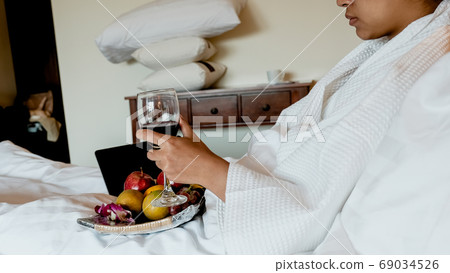 Picture of tourists holding wine, used laptop and eating fruits on the bed, health food concept Picture of tourists holding wine, used laptop and eating fruits on the bed, health food concept 69034526