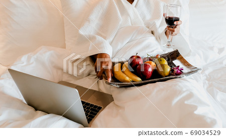 Picture of tourists holding wine, used laptop and eating fruits on the bed, health food concept 69034529