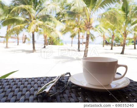 A cup of black coffee and sun glasses with coconut tree plan on white sand beach sea view background 69035240