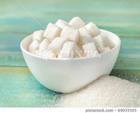 Bowl with sugar cubes on a turqoise wooden background 69035505