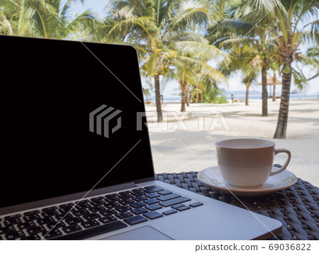 A cup of coffee beside laptop with Coconut tree and sea view, wh 69036822