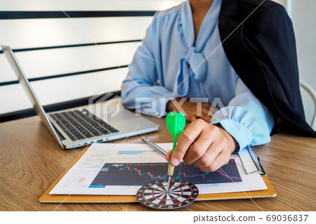 Trader woman holding a darts aiming at the target center of dart board Trader woman holding a darts aiming at the target center of dart board 69036837