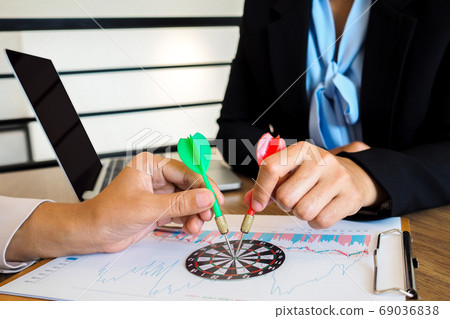Trader team holding a darts aiming at the target center of dart board Trader team holding a darts aiming at the target center of dart board 69036838
