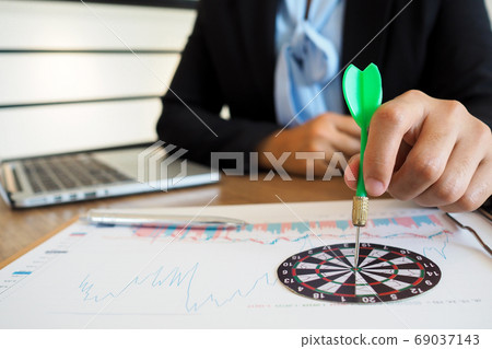 Trader woman holding a darts aiming at the target center of dart board 69037143