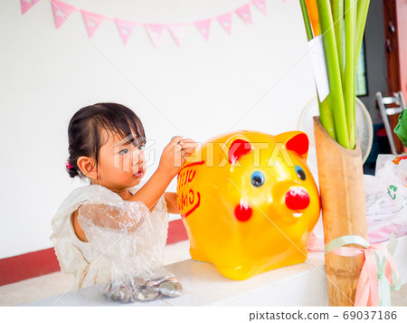 The little girl hand putting coin in the golden piggy bank received at a birthday party The little girl hand putting coin in the golden piggy bank received at a birthday party 69037186