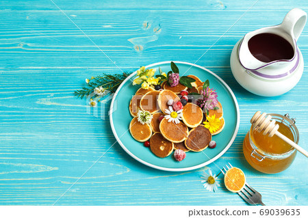 small pancakes with berries on a blue plate. With a jug of syrup and a jar of honey. On a blue wooden background, with space 69039635