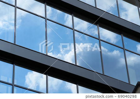facade of a modern building on a bright Sunny day, blue sky and clouds reflecting in a glass, beautiful exterior of the new building 69040298
