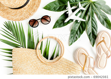 Woman's beach accessories: rattan bag, straw hat, tropical palm leaves, airplane on white background. The concept of travel. Summer background. Woman's beach accessories: rattan bag, straw hat, tropical palm leaves, airplane on white background. The concept of travel. Summer background. 69042081