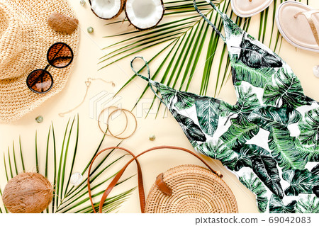 Woman's beach accessories: swimsuit with tropical print, rattan bag, straw hat, tropical palm leaves on yellow background. Summer background. Woman's beach accessories: swimsuit with tropical print, rattan bag, straw hat, tropical palm leaves on yellow background. Summer background. 69042083