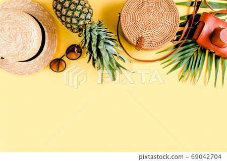 Women's accessories traveler: bamboo bag, straw hat, tropical palm leaves monstera, retro camera on yellow background. Flat lay, top view 69042704