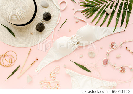 Feminine white swimsuit beach accessories, tropical palm leaf branches on pink background. Travel vacation concept. Summer background. Road frame set Feminine white swimsuit beach accessories, tropical palm leaf branches on pink background. Travel vacation concept. Summer background. Road frame set 69043100