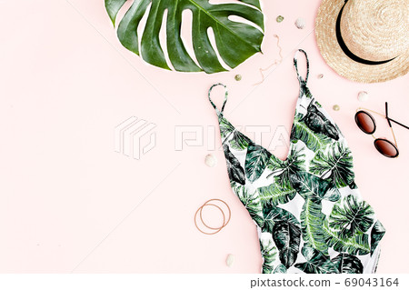 Woman's beach accessories: swimsuit with tropical print, straw hat on pink background. Summer background. Flat lay 69043164